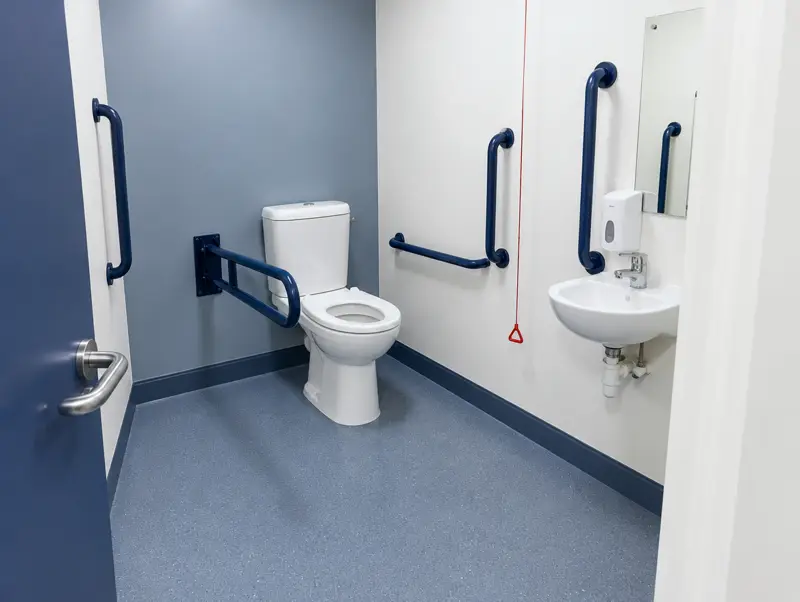 Accessible toilet room with contrasting grab rails and a drop-down support rail