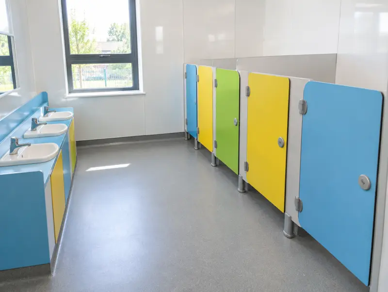 Junior school toilet cubicles with blue, yellow and green doors and low basins