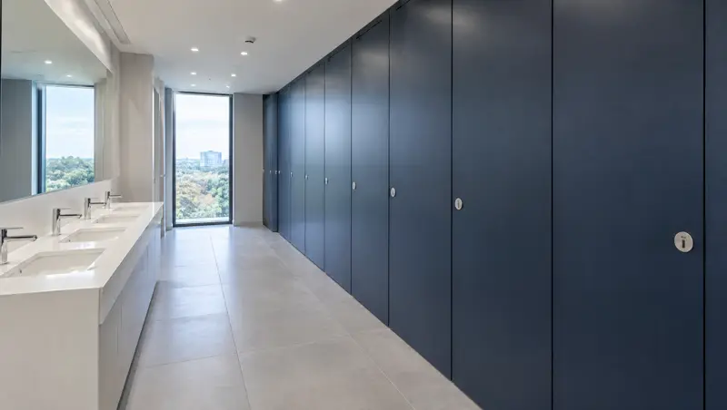 Run of floor-to-ceiling navy blue toilet cubicles with a solid-surface vanity in an office washroom